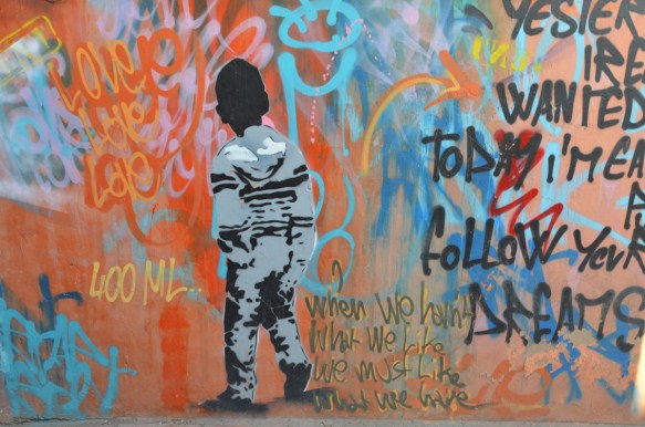 middle section of a mural by 400 ml in Marrakech, a boy in black and grey, back turned, against wall of bright reds and blues with words, love, love, love as well as 