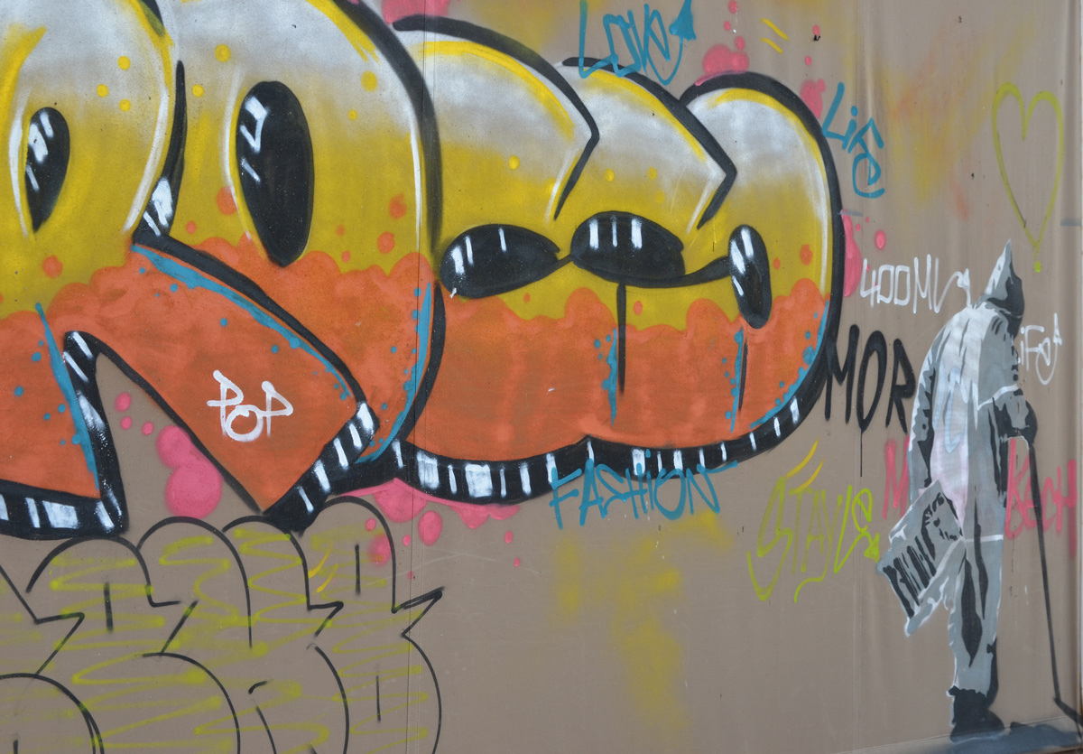 in a mural, an old man with a can and long grey coat with hood walks away, plus large orange and yellow letters that spell Rocco