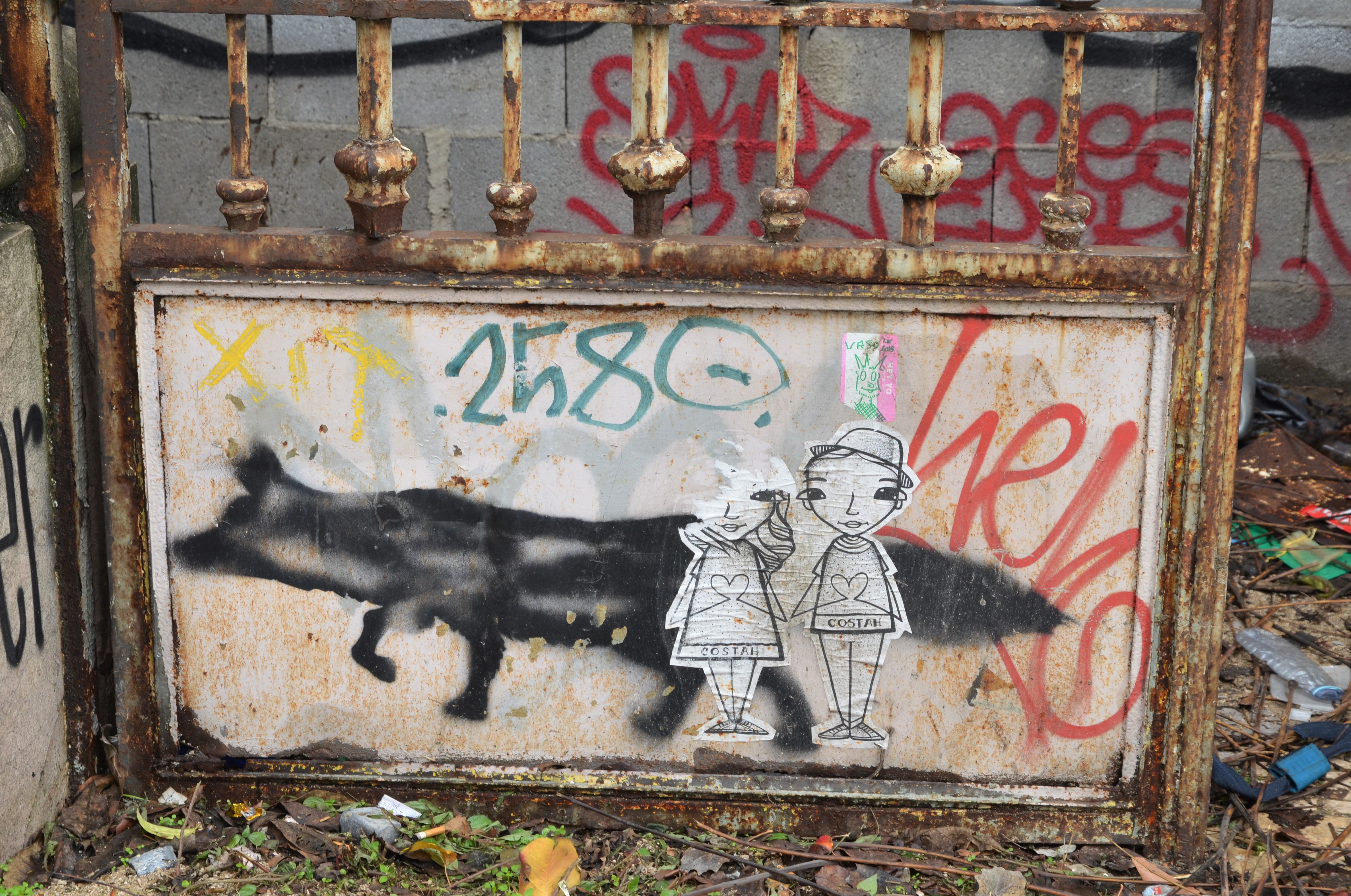 a black fox or wolf stencil on the bottom of a gate, along with a paste up of two people, a girl and a boy holding hands 