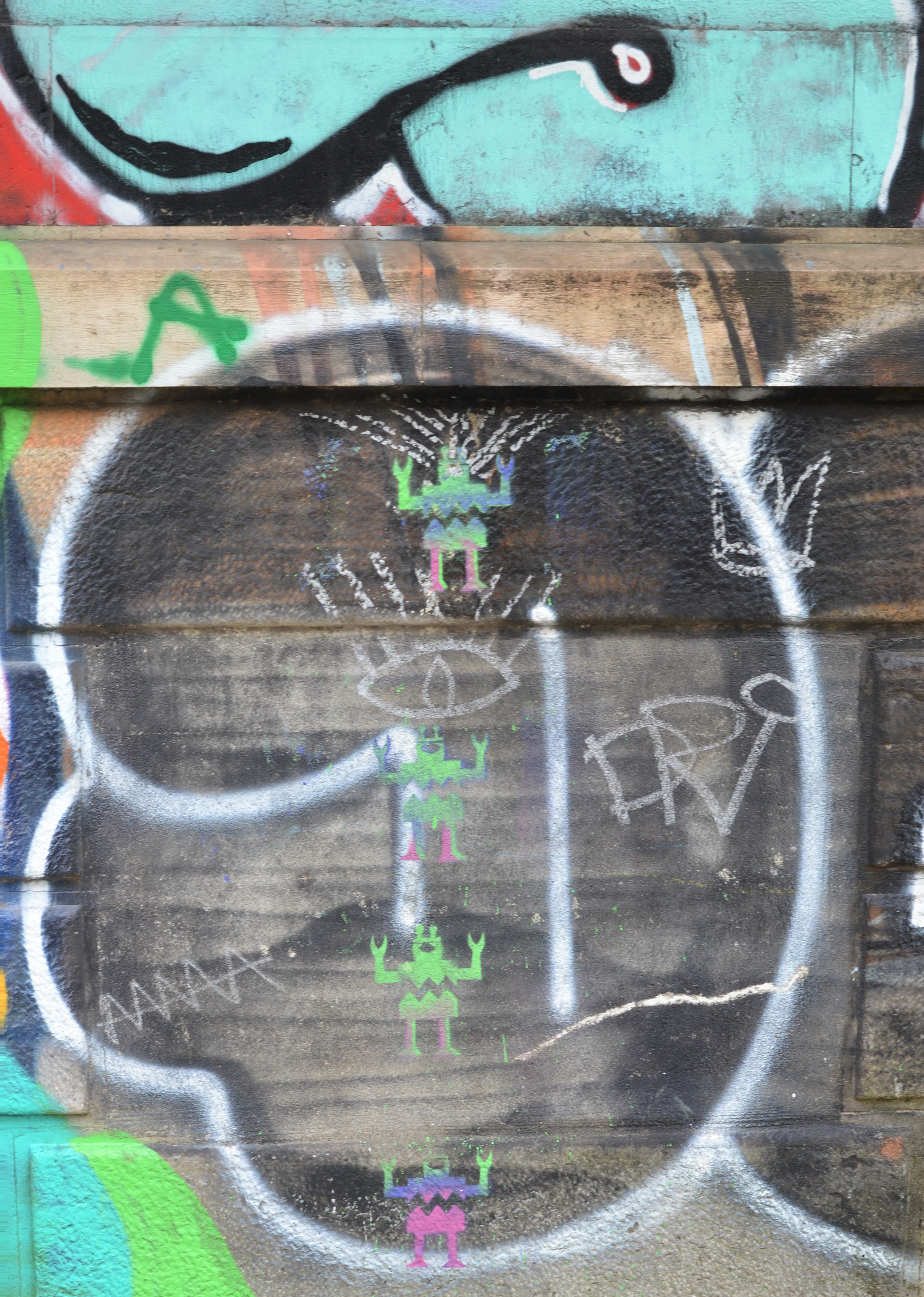 a black and white tag graffiti on a stone wall with some small green alien type figures stencil on top 