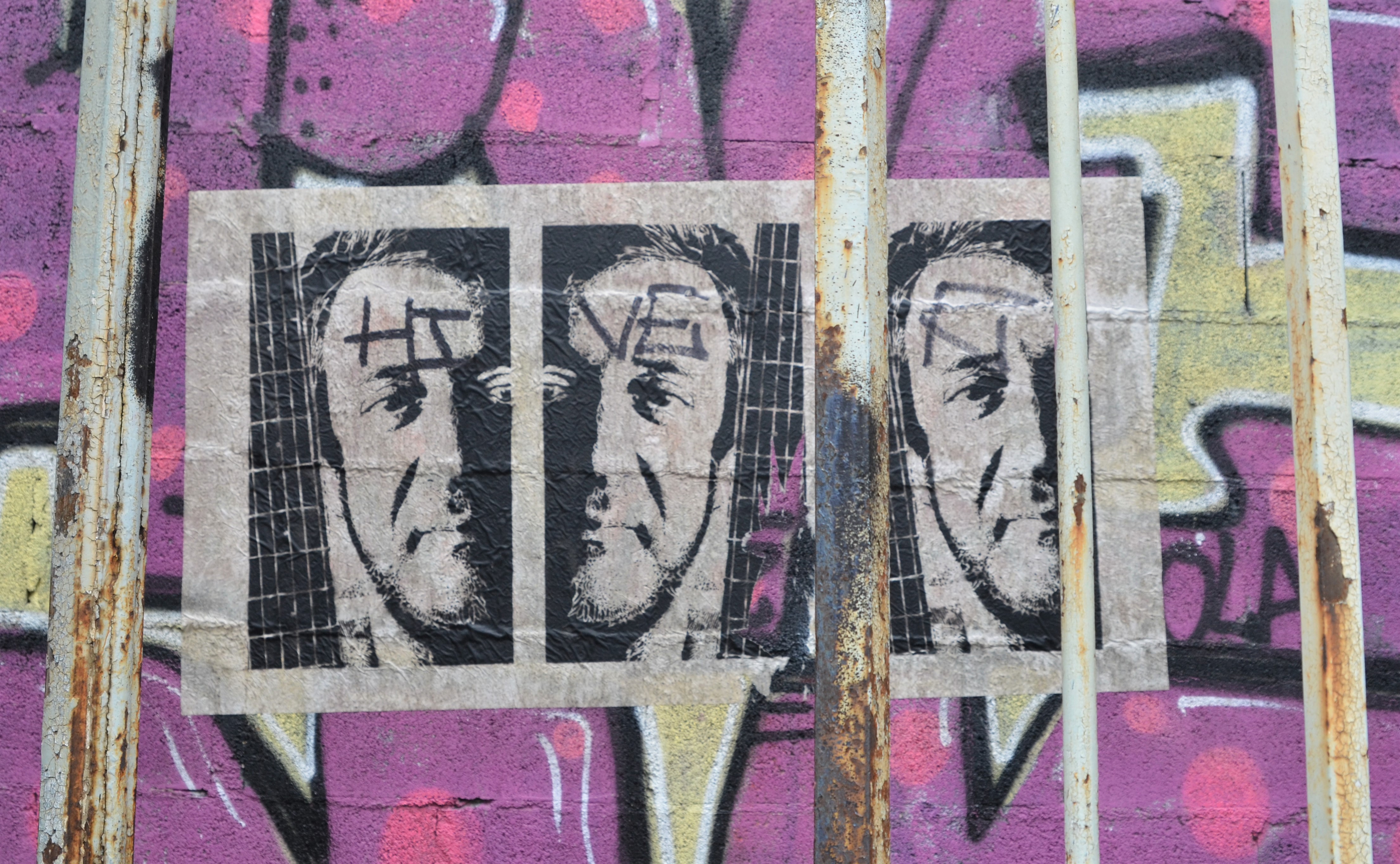 a pasteup of man's face in black and white, three copies of the same photo, on purple, behind bars of an old gate, stencil of singer Rui Veloso by A L Tony 