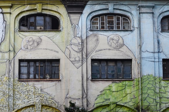 mural in Rome by Blu, on del porto fluviale, of large faces, where the eyes are windows in the buildings,