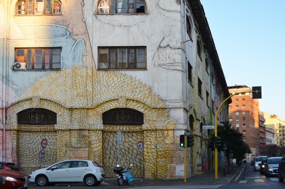 mural in Rome by Blu, on del porto fluviale, of large faces, where the eyes are windows in the buildings, at corner with via della conce