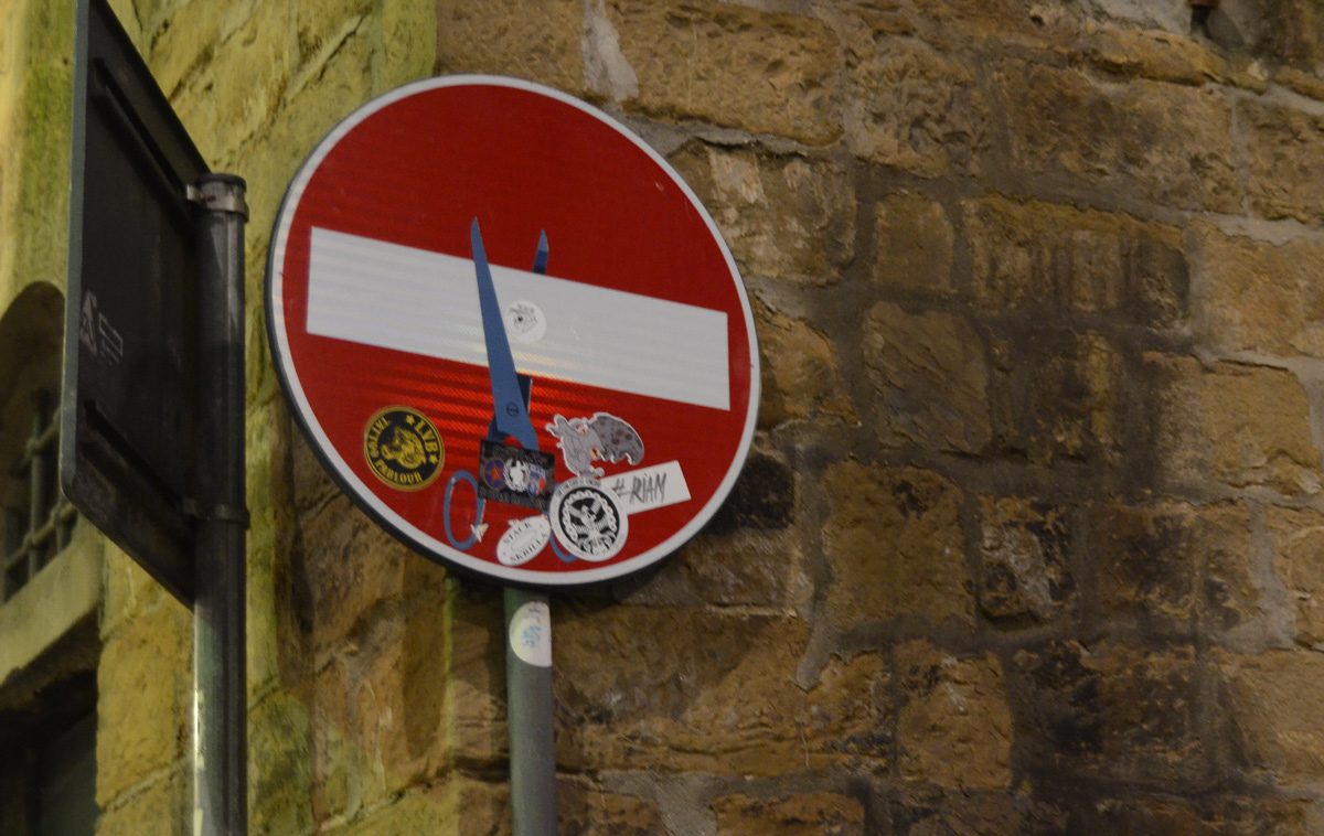 altered red and white no entry sign, graffiti by Clet Abraham, of a pair of scissors cuttig the white bar
