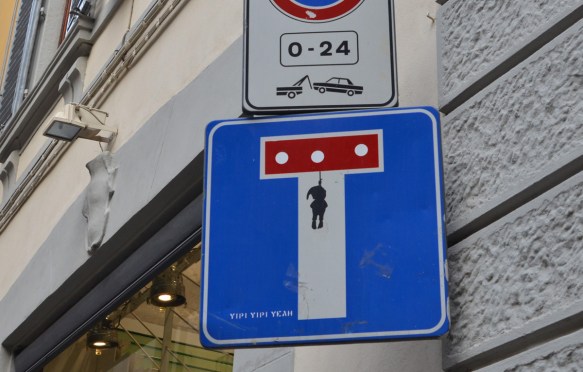 dead end sign altered by yipi yipi yeah, three holes in the red bar and a creature hanging by the neck