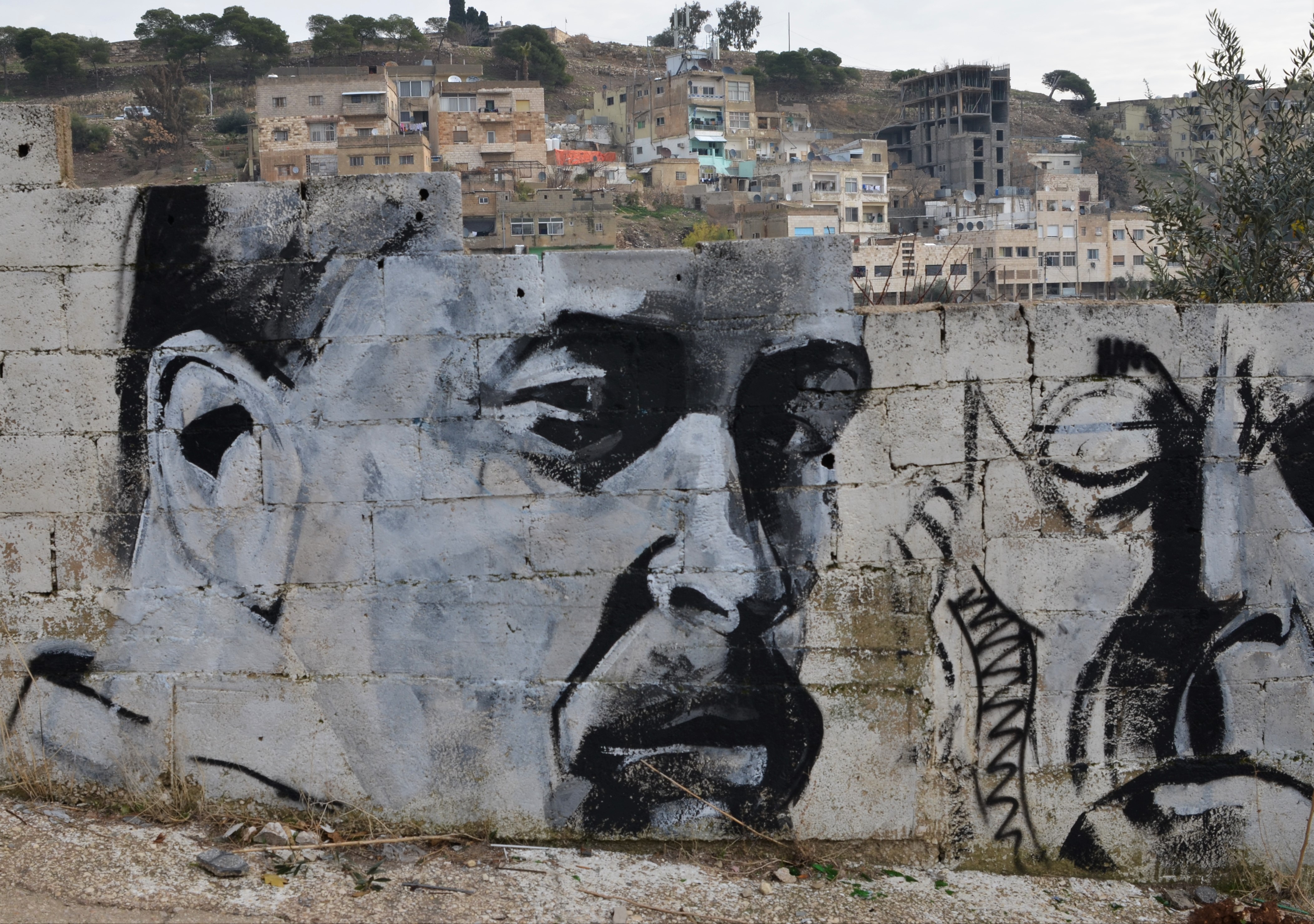 Black and white, grey tones, painting of a man's face in partial profile, on a wall. Can see the city beyond over the top of his forehead 