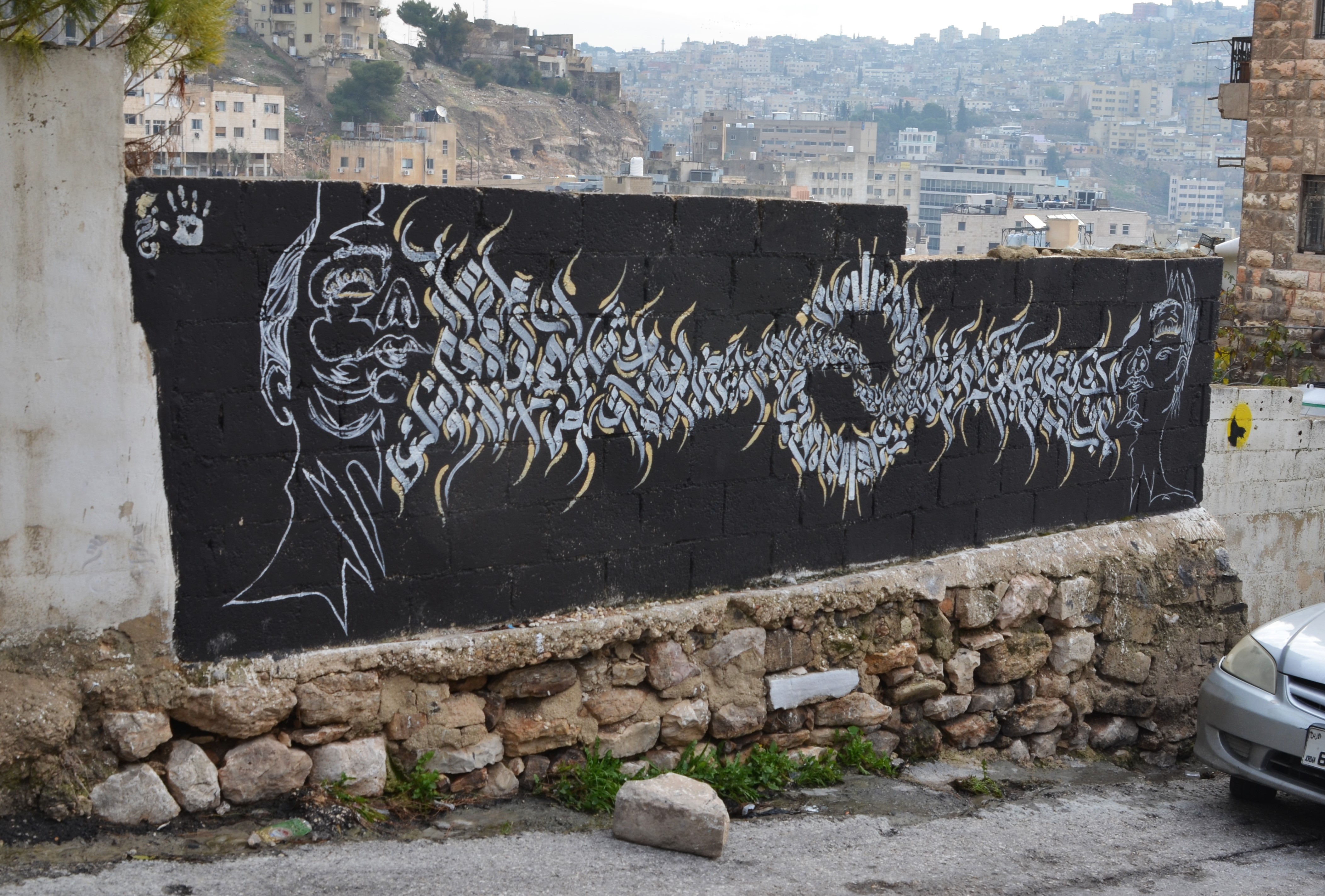 black and white mural of two faces, one at each end, with arabic letters between them 