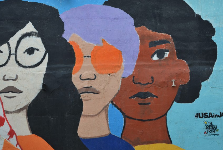 three large facecs in a mural, one with orange sunglasses and purple hair, one Asian looking with large black glasses