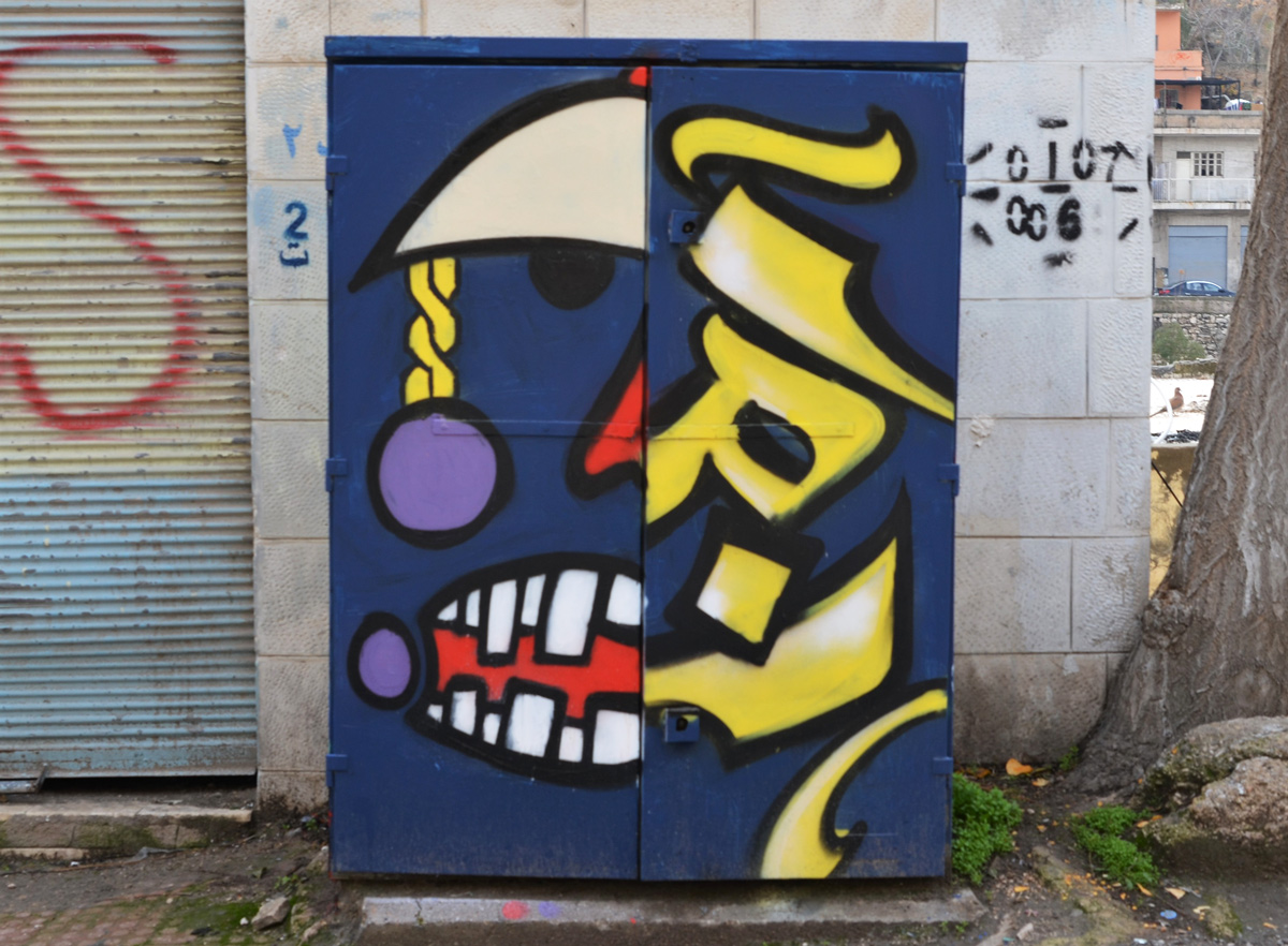 metal box on street painted, dark blue background, left half is half a face while right side is Arabic letters in yellow