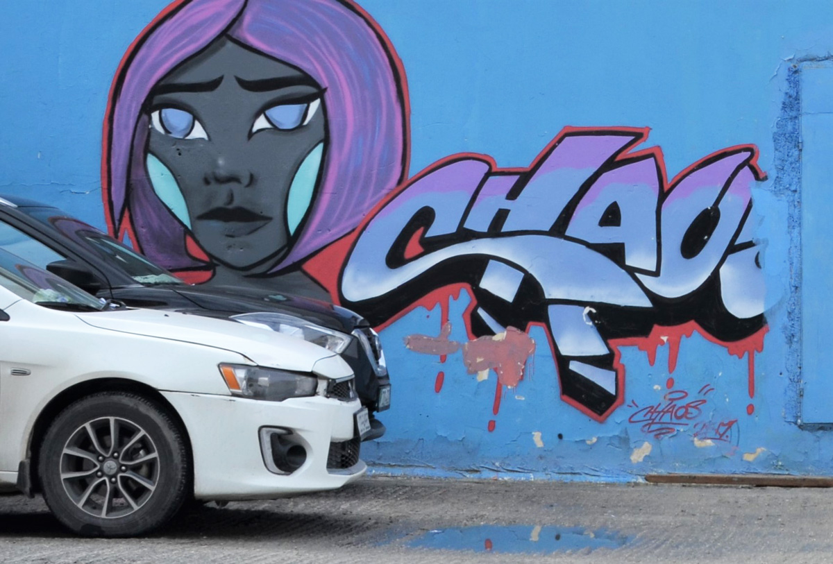 white car and black car parked in front of mural with a woman's face, purple hair, and text that says chaos