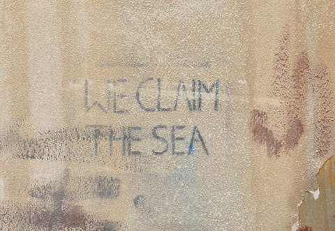 stencil on a wall, black letters that say we claim the sea