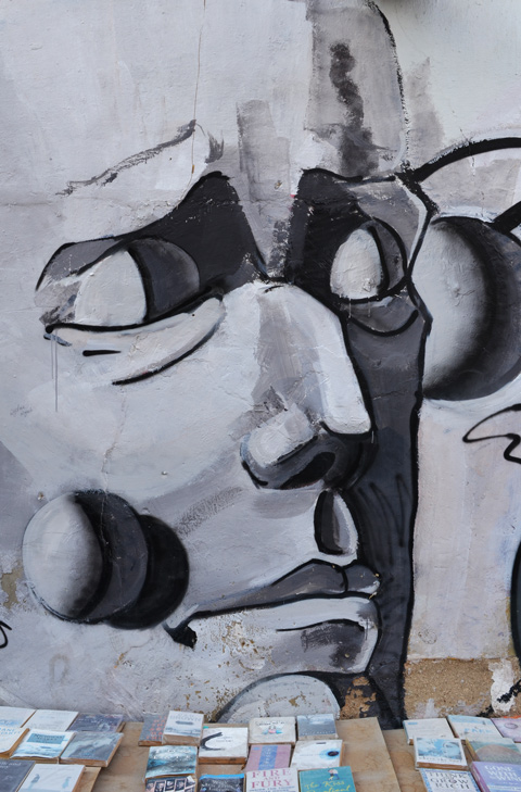 shades of grey, stylized man's face on a wall behind a table with books on it