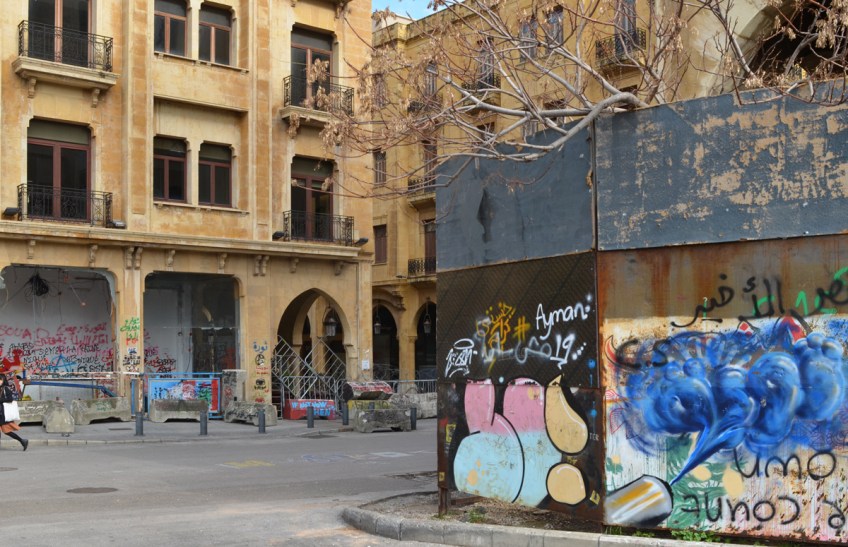 on a city street, low rise goldish brown stone buildings with graffiti and street art around the bottom layer