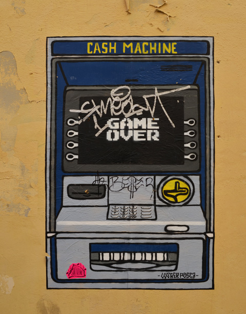 paste up graffiti on a wall in Rome, a picture of a cash machine as video game, monitor says game over