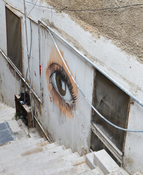 realistic painting of an eye on a wall between two windows on a set of stairs