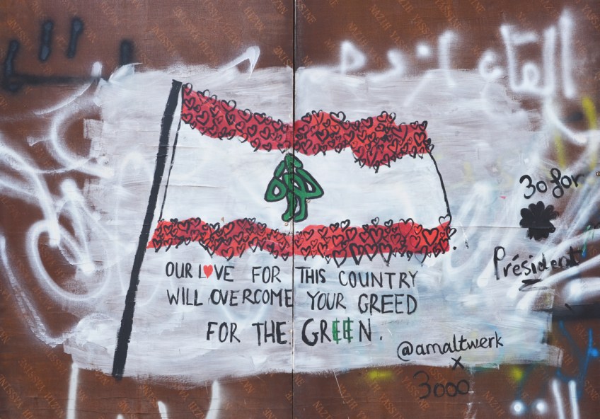 street art of a Lebanese flag with the red stripes made of hearts, also the words Our Love for the country will overcome your green for the green