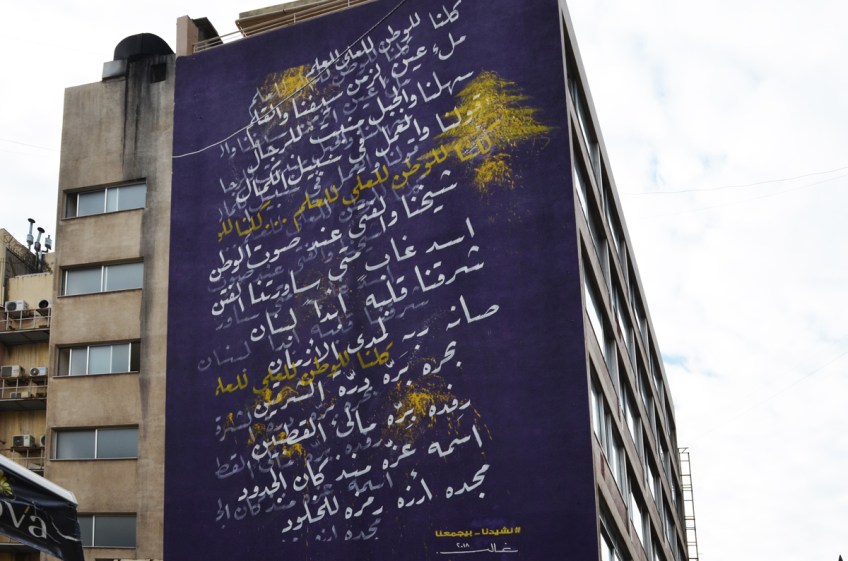 large mural on the side of a building in Hamras Beirut, purple background with white Arabic writing on it