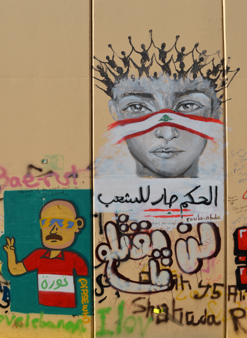 a head with stick figure people with arms upward as hair, and a strip of cloth in form of Lebanese flag across bridge of nose and cheeks, by Roula Abdo alongside a man in a red and white shirt on a green background, both graffiti on a wall 