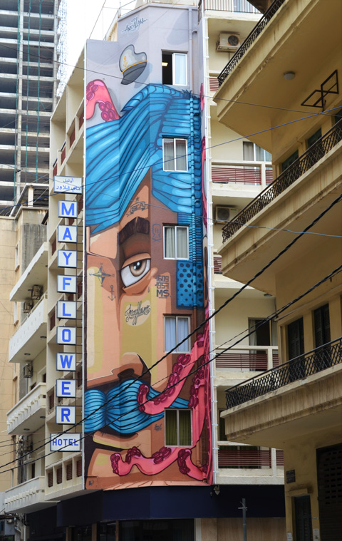 tall narrow mural of part of a man's face, with blue hair and blue mustache, by apocaleps