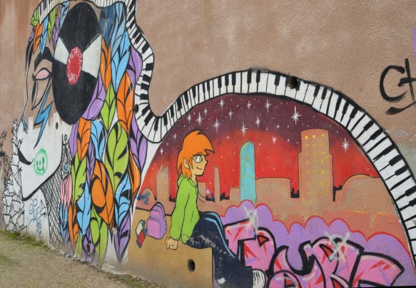 mural by Suha Sultan of a woman with a vinyl record on the side of her head, piano keys covering the top of the mural, a young boy sitting beside a cityscape behind the woman, 
