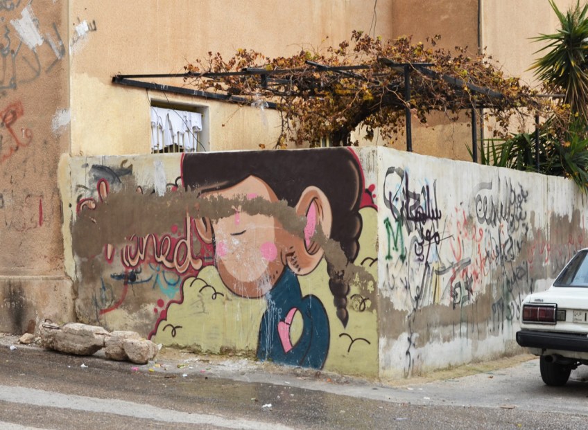 muddied old mural on a wall around a courtyard, a car parked beside