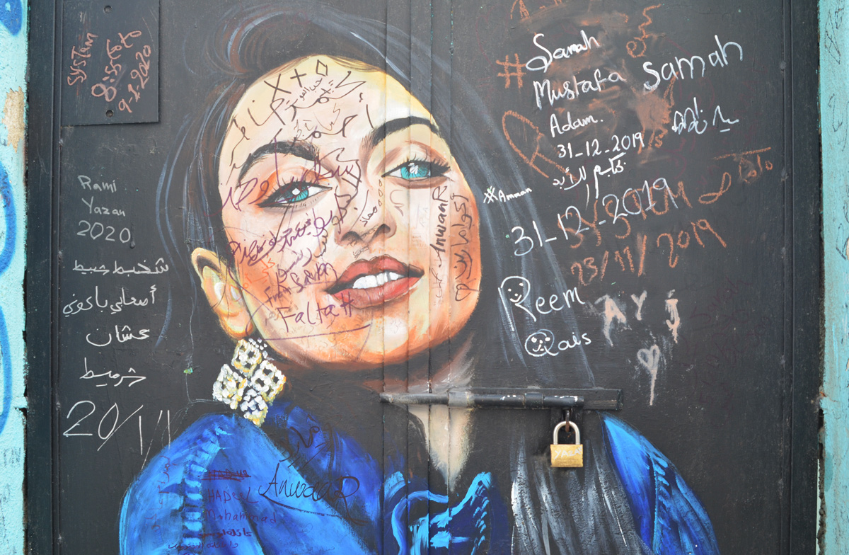 painting of a woman in a blue top on a black wall, that people have written their names on 