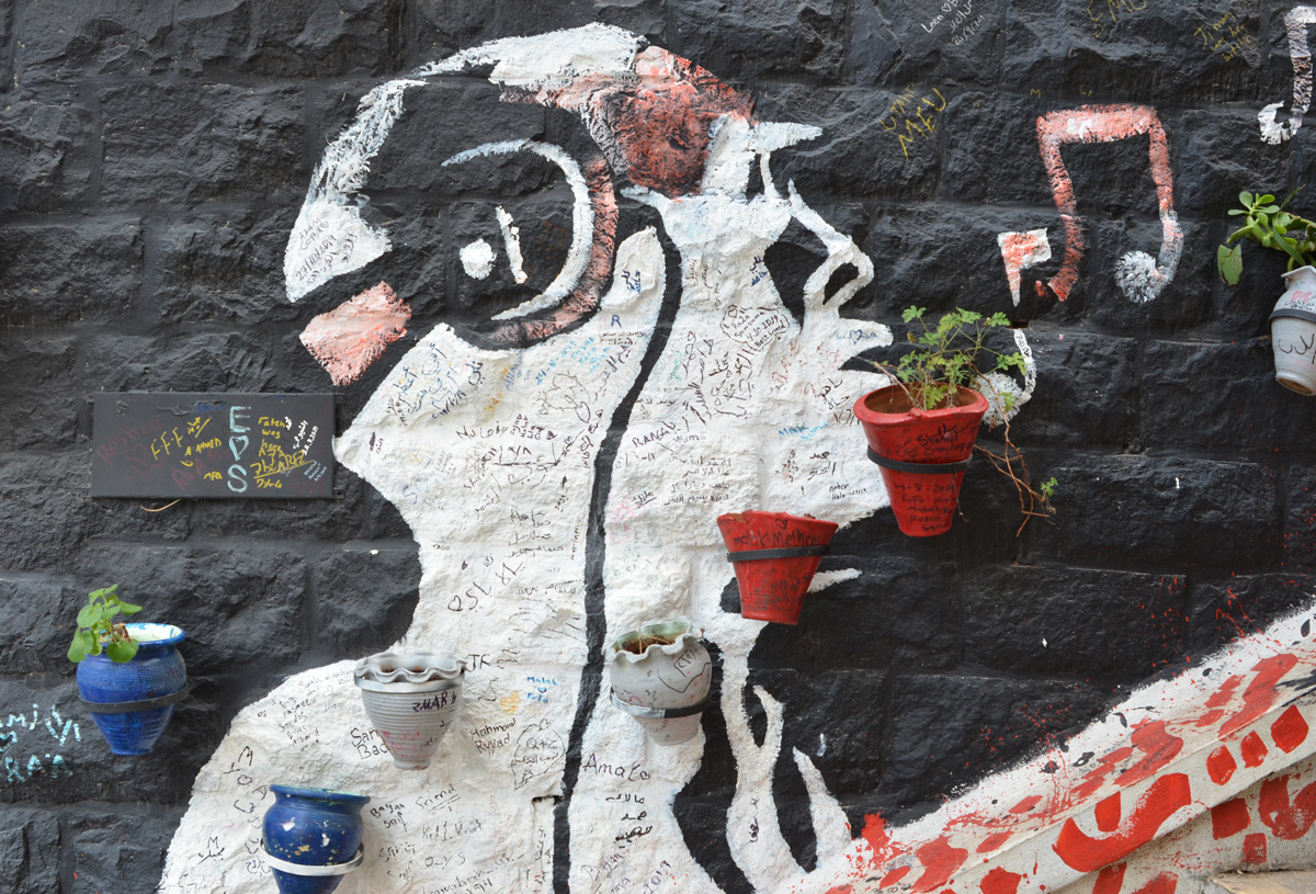 on a black wall, a profile silhouette in white of a man with headphones on, plants in terra cotta planters line the stairs that run beside the wall 