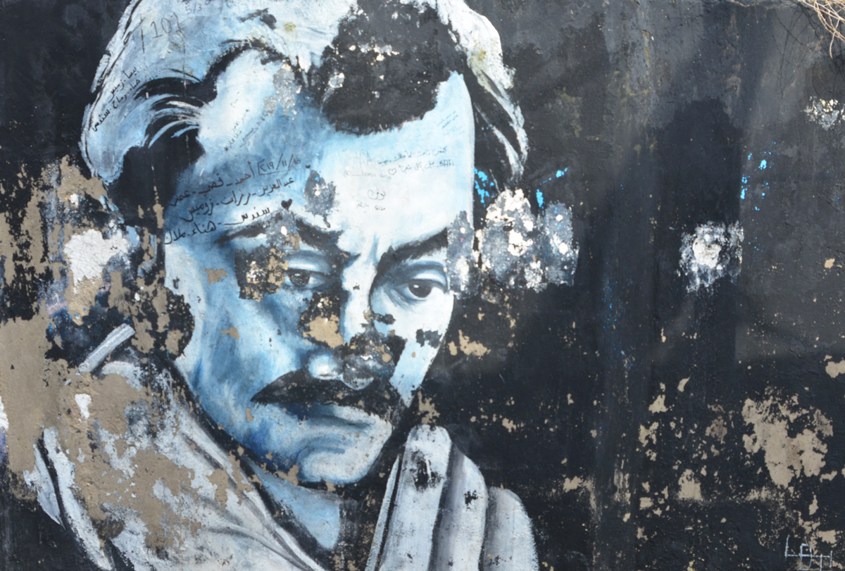 black and white street art painting of Omar Shariff on a black background, some of the paint has begun to peel off