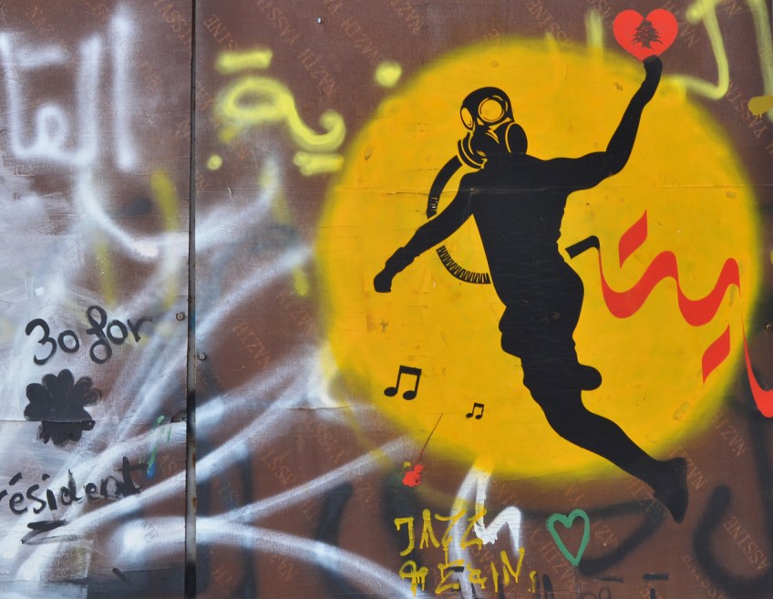 graffiti of a yellow circle with black silhouette of a person with a gas mask on, throwing a red heart