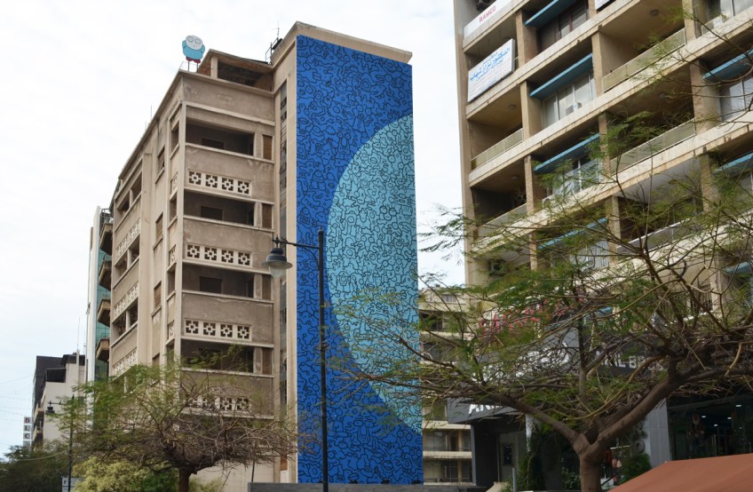 multi storey residential buildings, one has a large mural on the side of it, blue with a lighter blue semi-circle, with Arabic writing over it