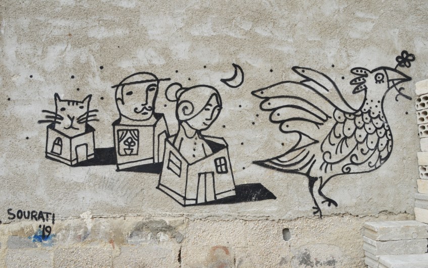 small street art on a concrete wall, whimsical drawings by sourati of people in small houses withtheir heads sticking out of the roofs , a moon in the sky and also a cat sticking its head out of a small house,