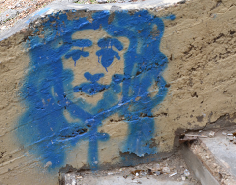 a blue graffiti painting on a wall, down low near the ground, of a man with beard and long hair.