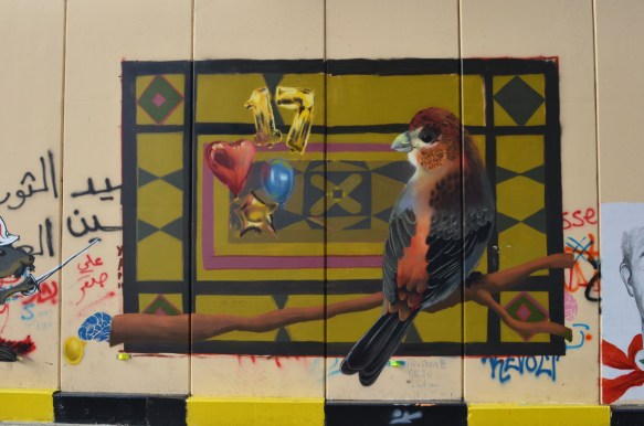 realistic painting of a red and black bird on a branch, on a wall in Beirut