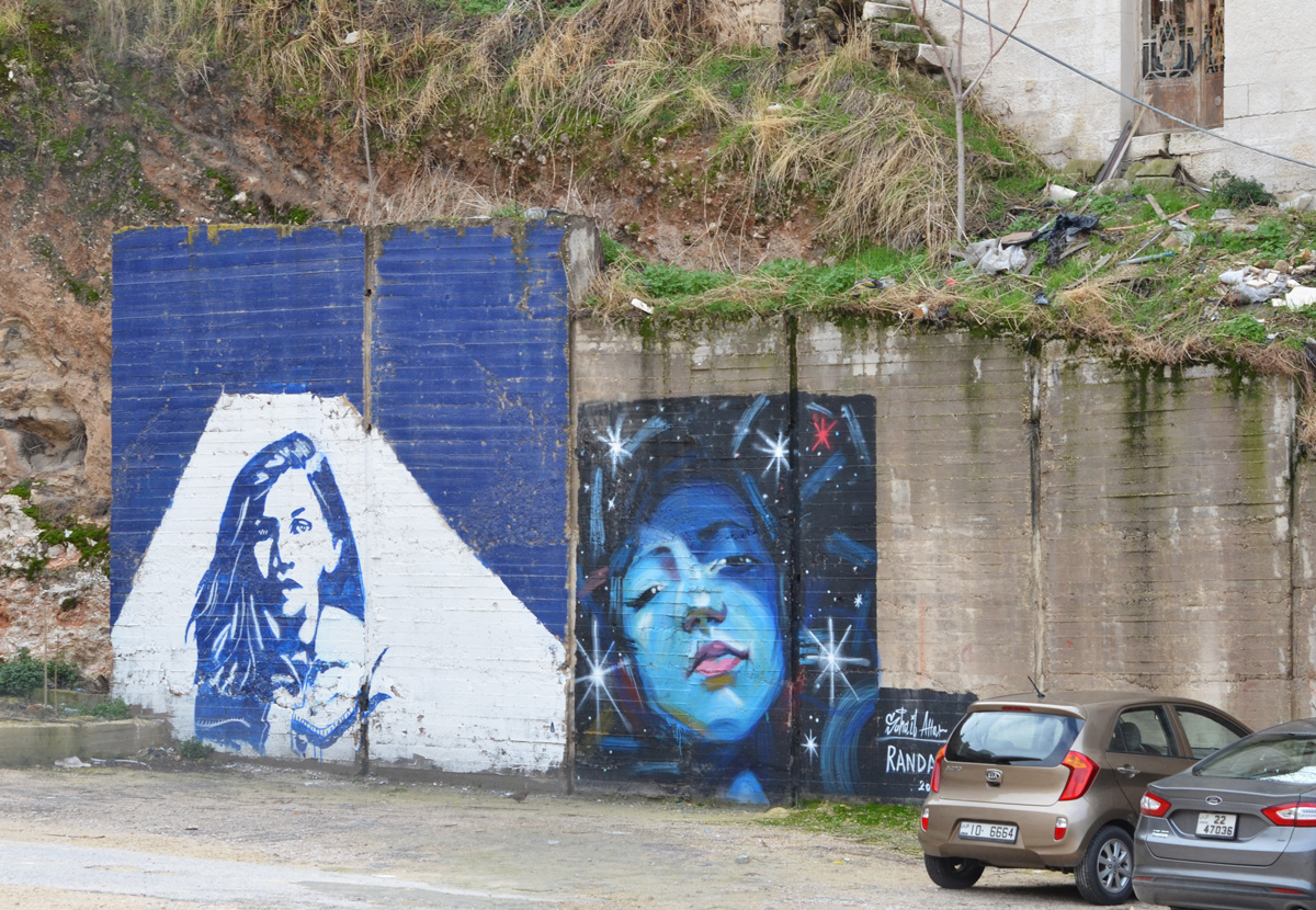 two murals of women. on the left is a portrait in blue and white of a woman with long hair. on the right is a Suhaib Attar painting of a woman's face surroundd by stars