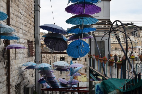 man blue, teal, and purple umbrellas, open, up high to provide shade over a set of stairs in Amman
