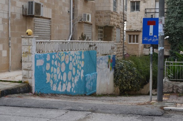 on a wall beside a driveway, a blue and white graffiti 
