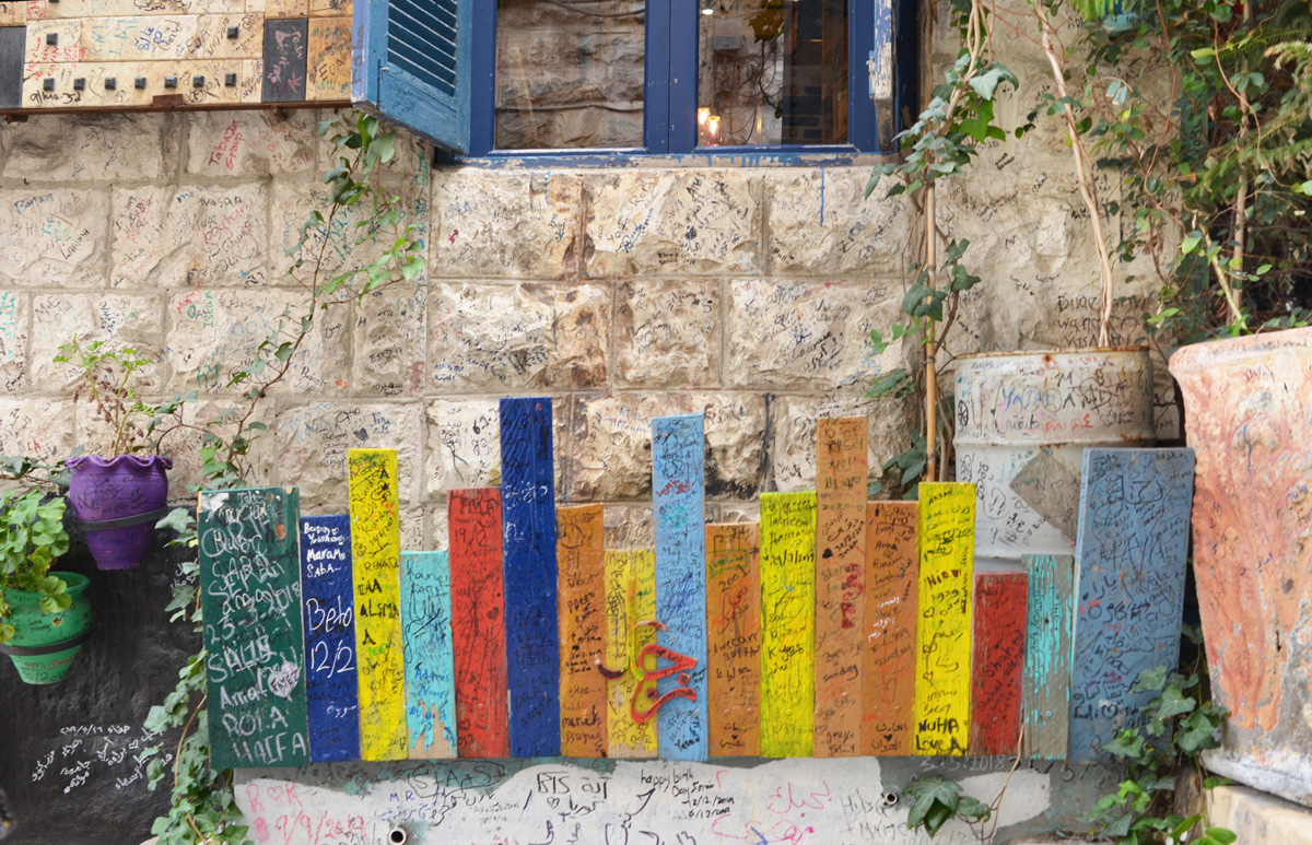 on a wall, under a window with a blue frame, a line of flat pieces of wood painted in bright colours, that look like a row of books 