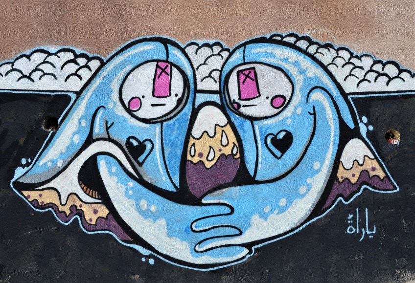 street art on a wall in Amman,- two blue stylized characters with arms curved towards each other and holding hands