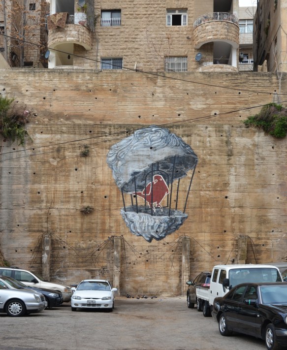 red bird in a birdcage, mural on a wall by a parking lot 