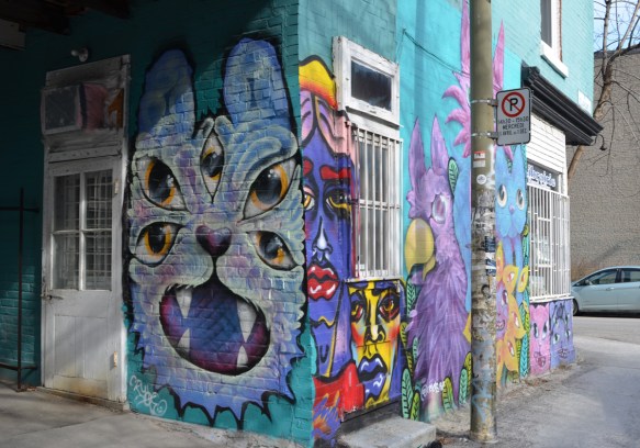 a light purple cat with 5 eyes, mural on a wall, on a corner, with more cats and cats faces on the adjacent wall 