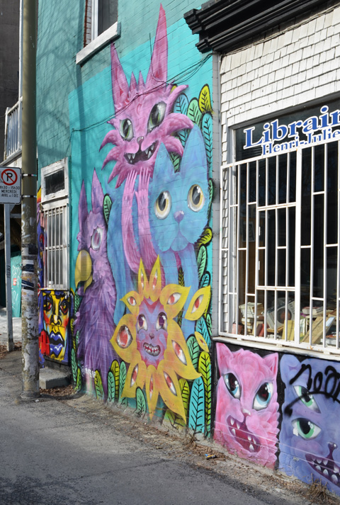 pink and blue cats mural on a wall beside a window, with a pink and blue cat faces under the window 