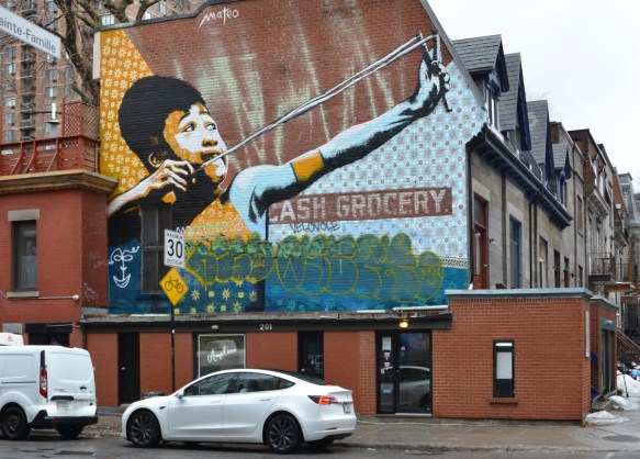 mural of a boy with a slongshot by mateo on the side of cash and grocery store on Milton St in Montreal