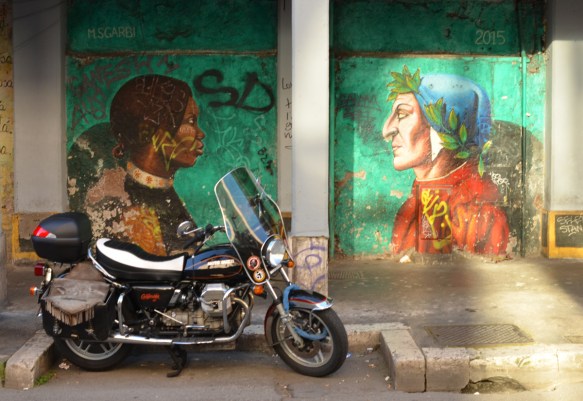 motorcycle parked in front of a wall with a mural by Mauro Sgarbi, green background, called Divine Welcome, Dante on one side, an immigrant woman on the other