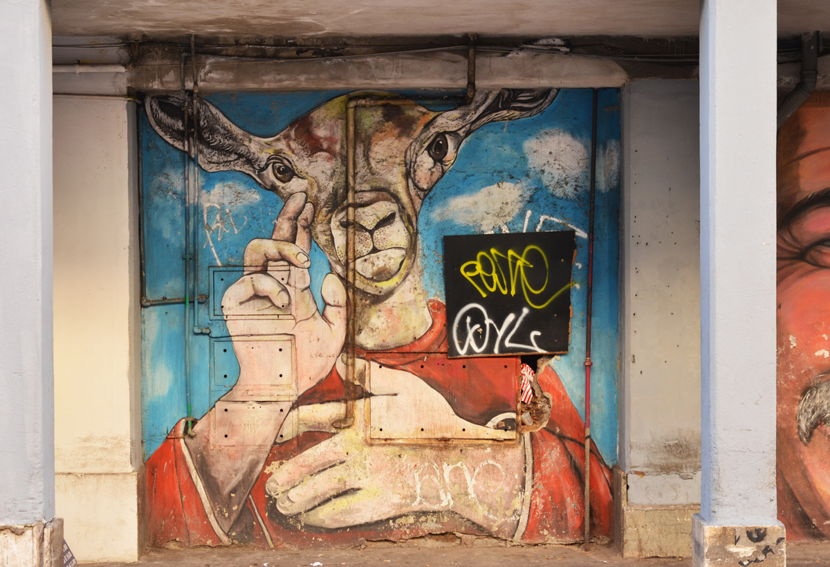 a mural of a person shoulders up except that there is a goat's head instead of a human head, arms and hands are human, wearing a red shirt, 