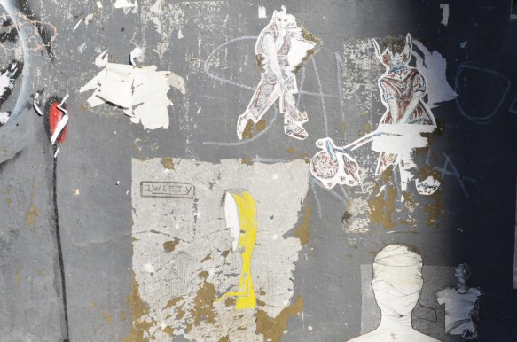 some old faded and partially torn wheatpaste paste ups on a grey wall 