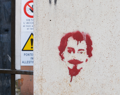 a red stencil on a concrete wall of a man with goatee