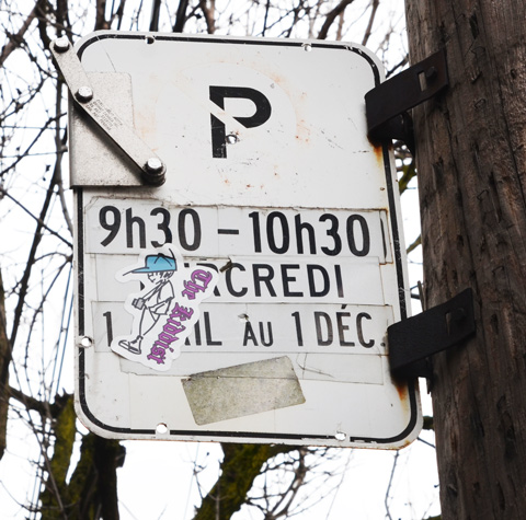 a parking street sign with a sticker on it of a boy with a camera around his neck and the words the kiddist