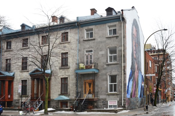 a large mural of a woman on the side of a row of old stone houses