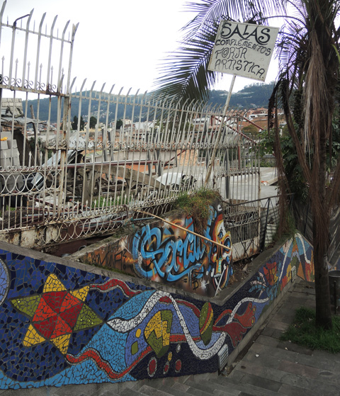 staircase outside, wall is covered with mosaics, with city beyond a wrought iron fence 