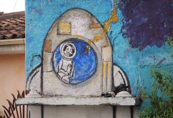 street art painting of an astronaut with a helmet on inside the round window of a rocket